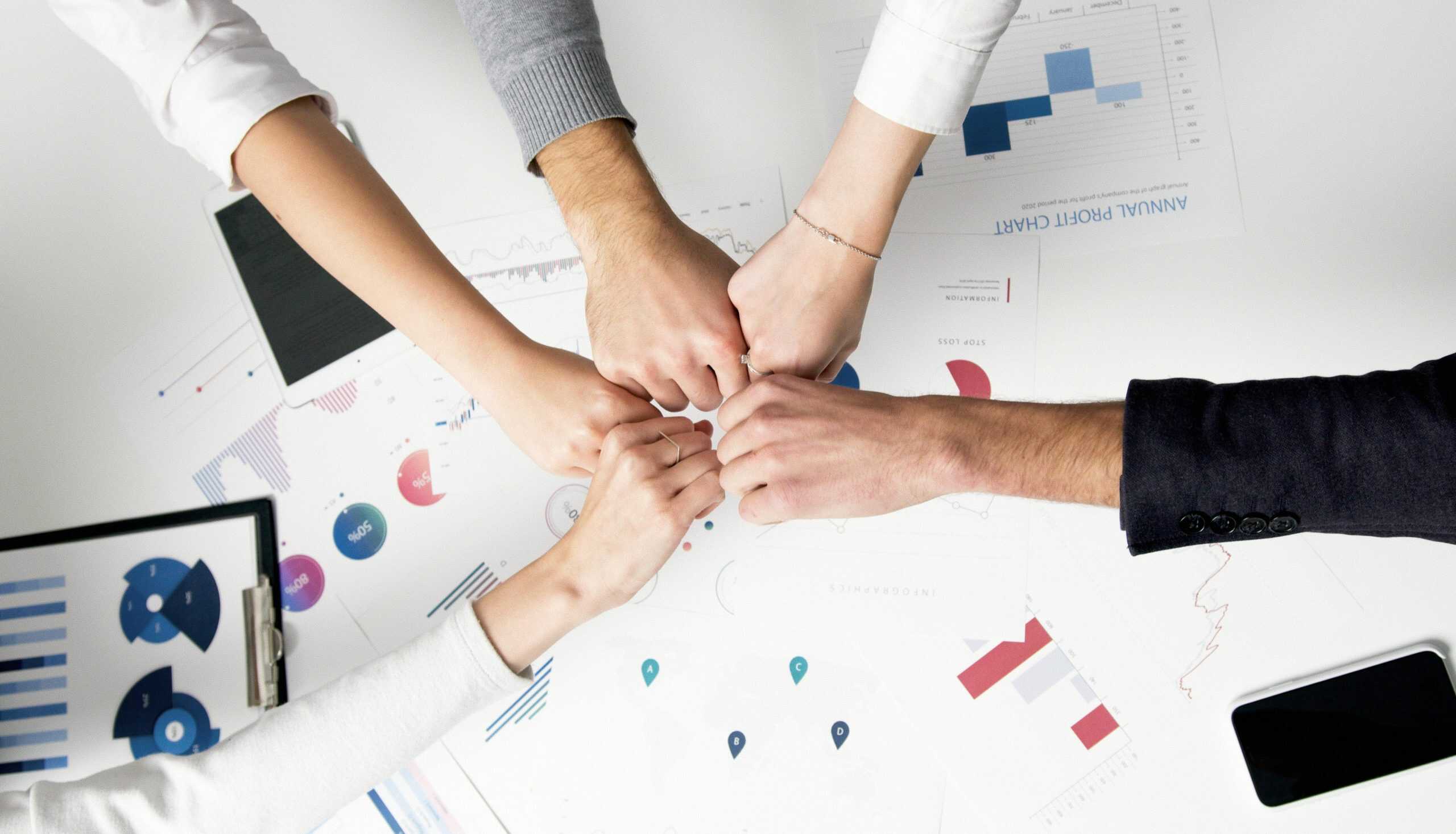 Team members bumping fists over a desk covered with business reports, charts, and digital devices, symbolising collaboration and teamwork.