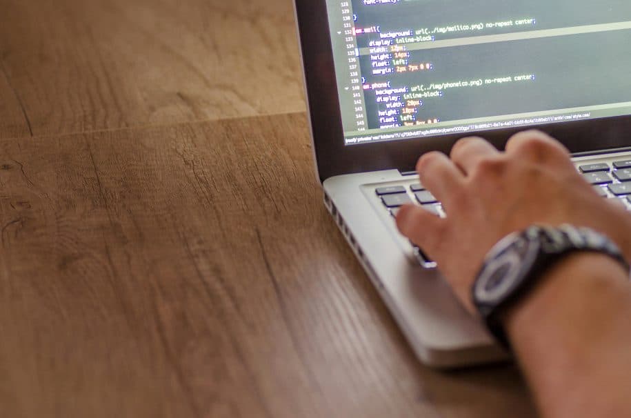 Hands typing on a laptop keyboard with lines of code visible on the screen.