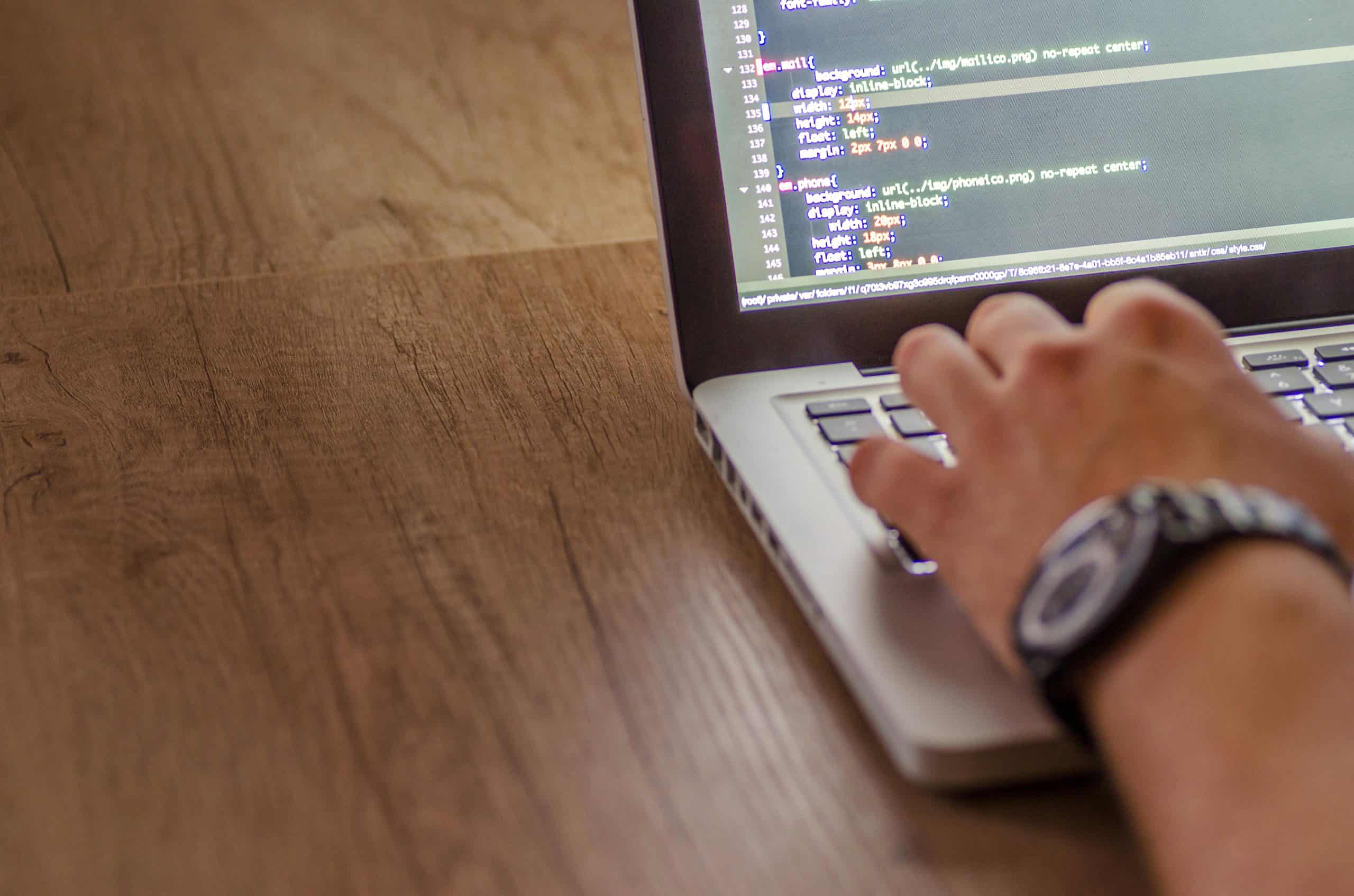 Hands typing on a laptop keyboard with lines of code visible on the screen.