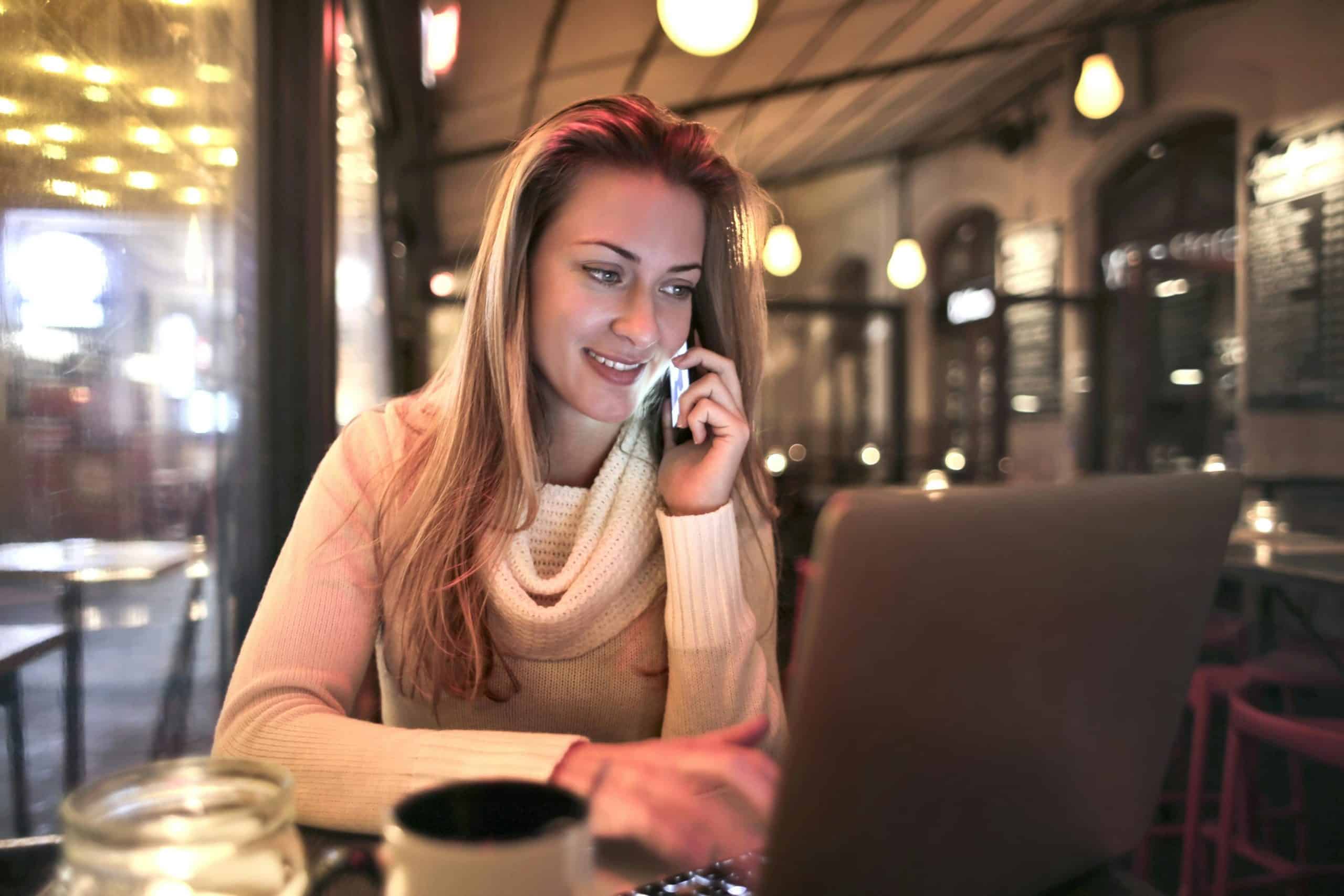 Woman using laptop and talking on phone for live chat support.