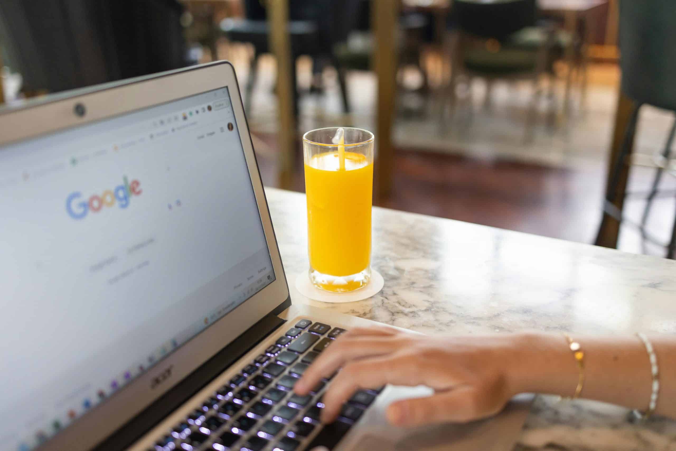 ALT: Laptop showing Google search with a glass of orange juice nearby for live chat monitoring.