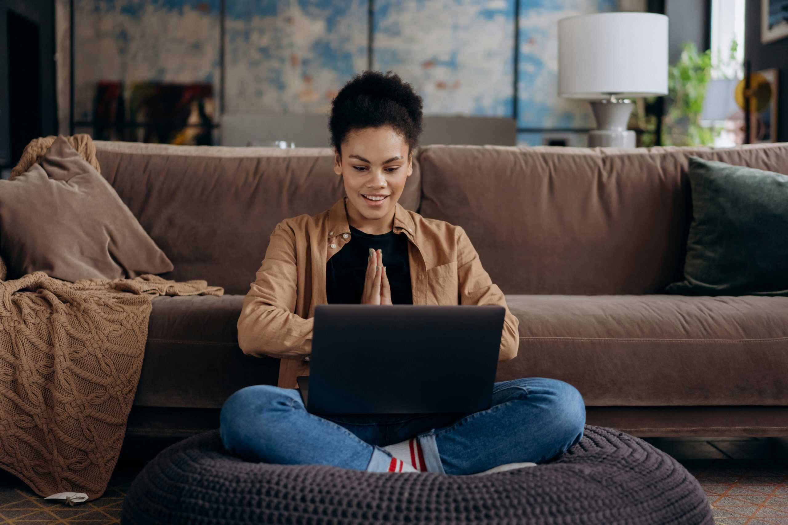 Young woman using laptop happily at home, enjoying live chat monitoring and customer engagement.