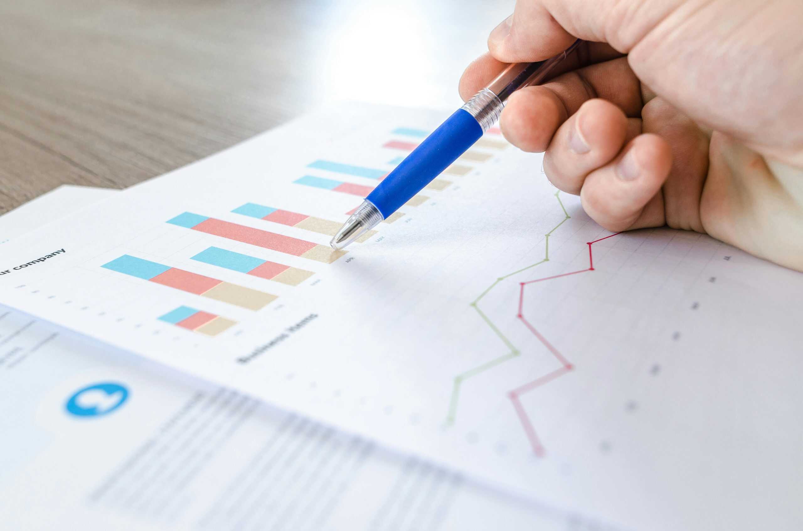 Hand holding pen pointing at data charts in report.