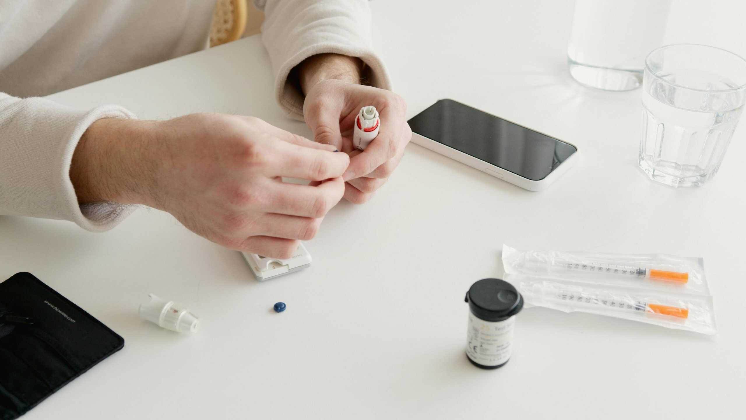Close-up of hands preparing medication at a desk with smartphone and medical supplies.