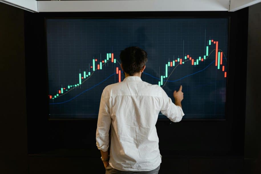 A person analyzing stock market trends on a large digital screen displaying candlestick charts for trading insights.