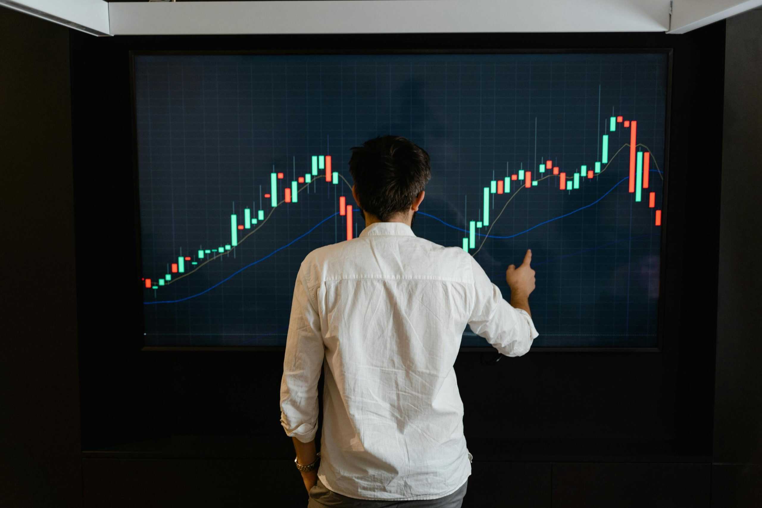 A person analyzing stock market trends on a large digital screen displaying candlestick charts for trading insights.