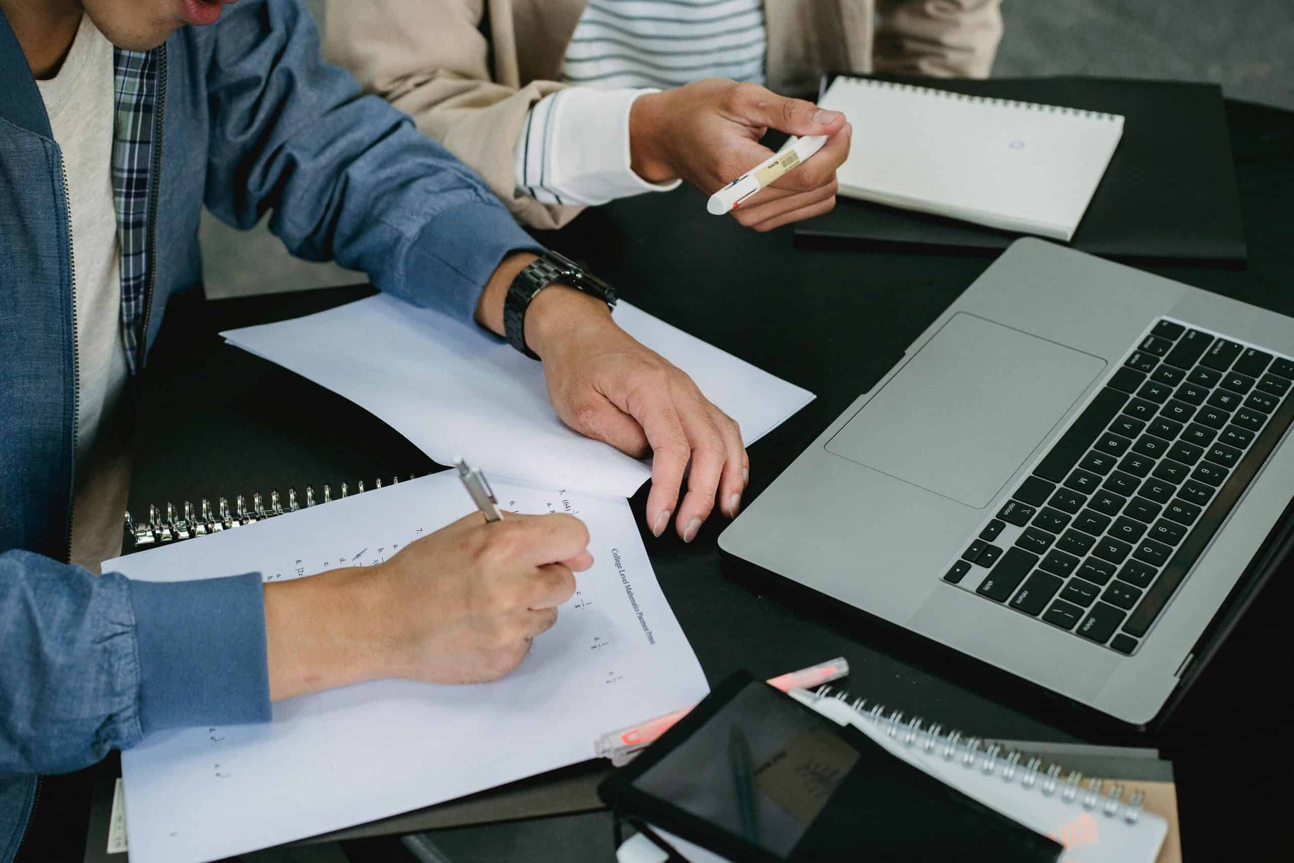 Close-up of people working together on live chat monitoring, analyzing customer interactions with a laptop and documents.