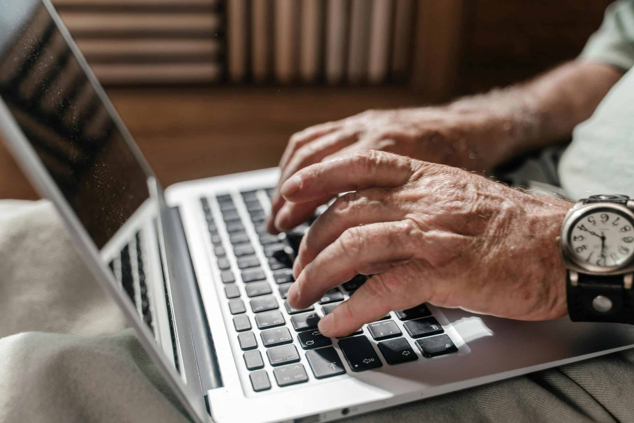 Elderly person using a laptop for live chat monitoring at home.