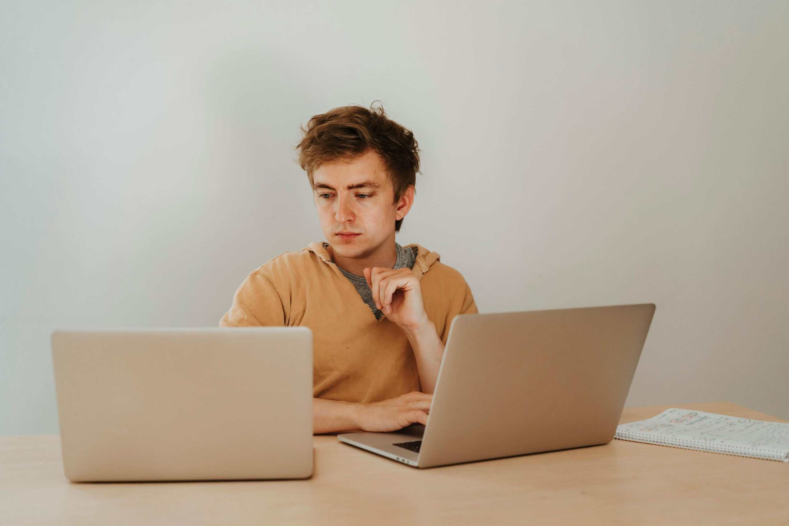 Young man monitoring live chat interactions on dual laptops for customer support.