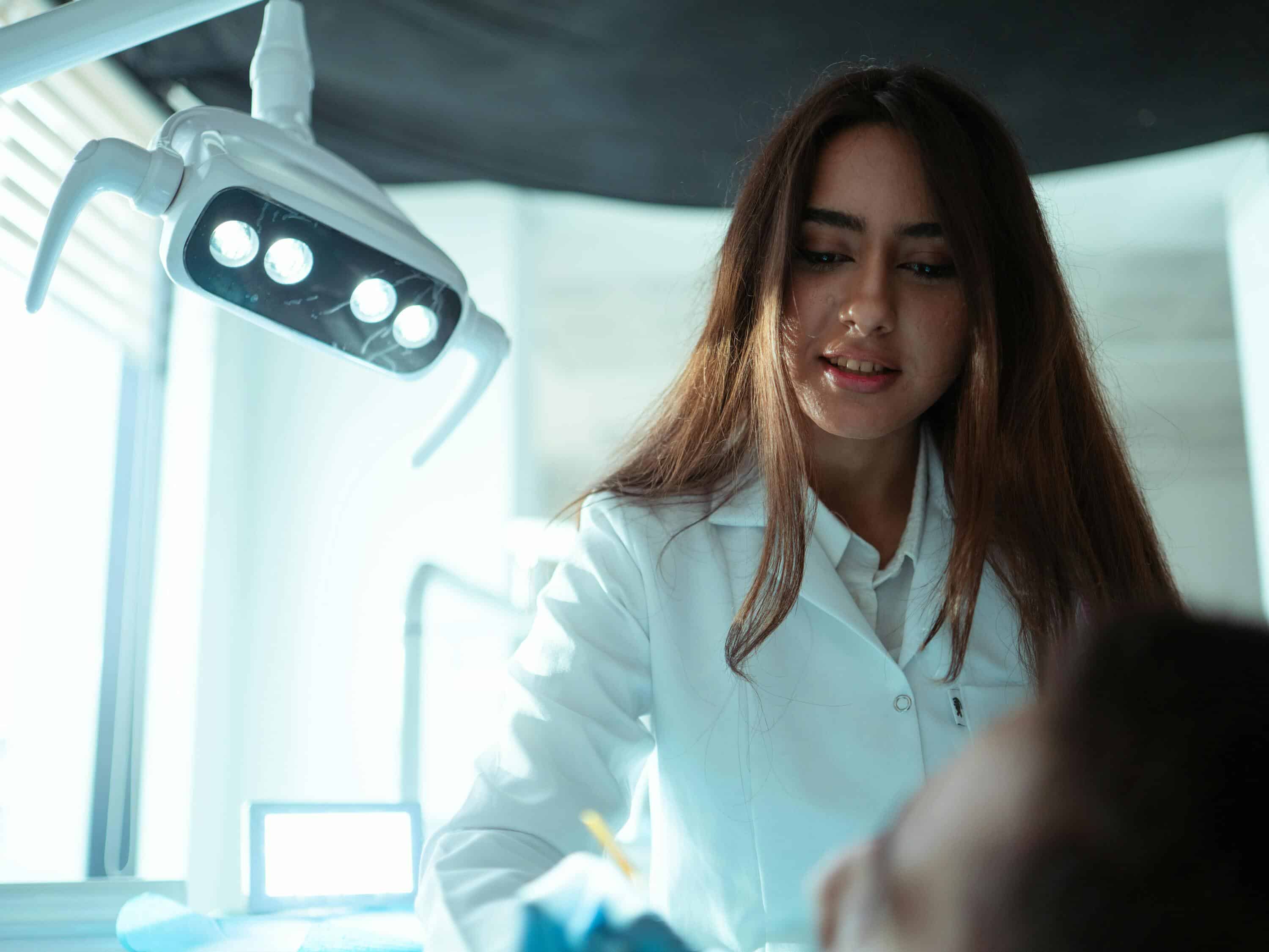 Woman monitoring live chat interactions in a medical setting with dental light overhead.