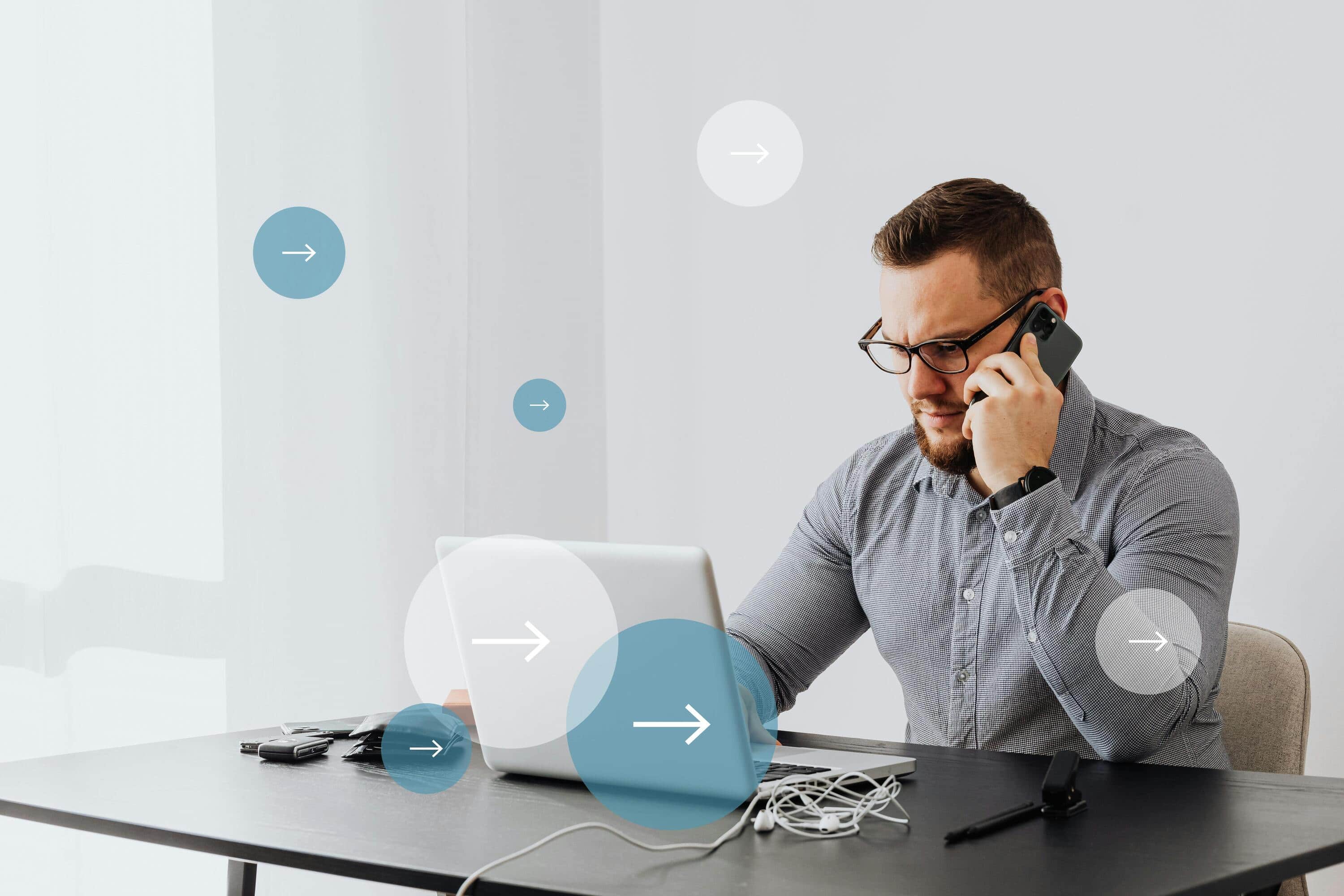 Man using laptop and phone for live chat monitoring in office.