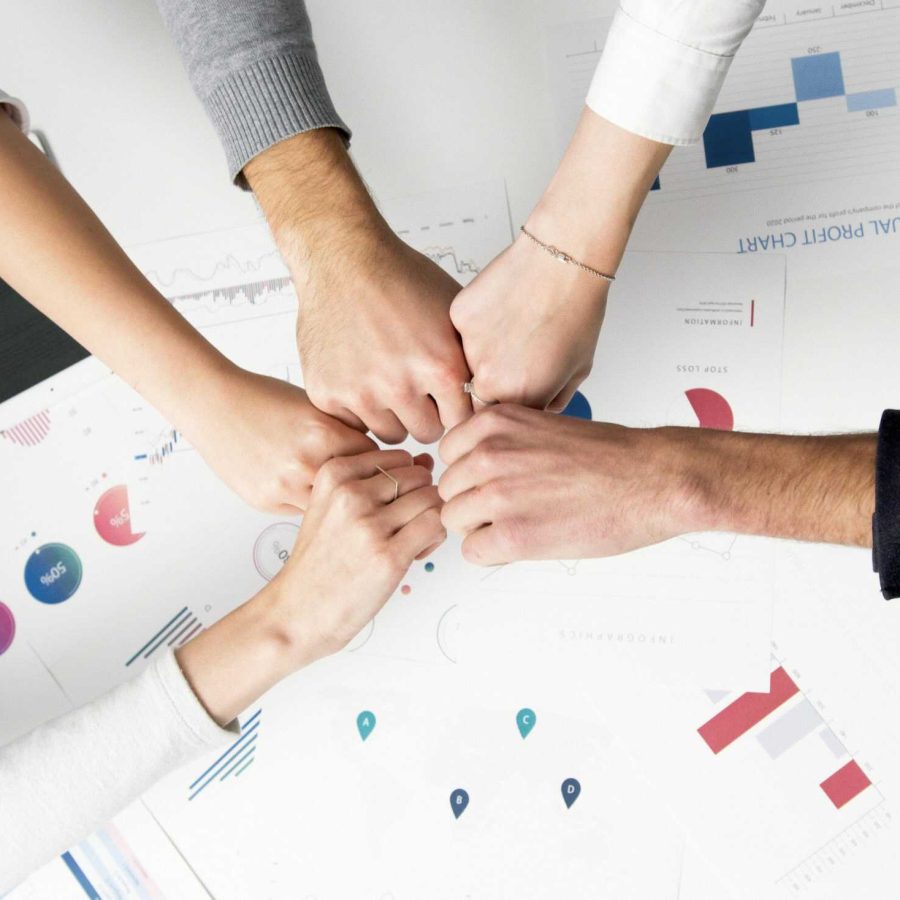 Team members bumping fists over a desk covered with business reports, charts, and digital devices, symbolising collaboration and teamwork.